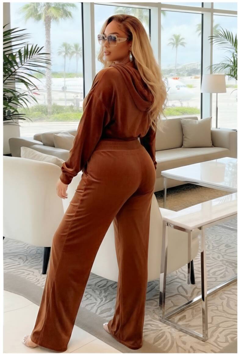 Swerves & Curves Boutique brown velvet hooded jogging set worn by a blonde woman in a luxury lounge setting.